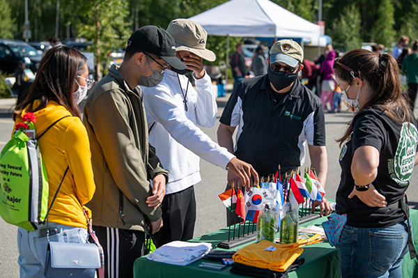 Brian Tang, Maezelle Tacas, and Lawrence Giron check out the Multicultural Student Services table with Student Success Coordinator Leo Medal at UAA's Fall 2021 Campus Kickoff outside the Alaska Airlines Center.