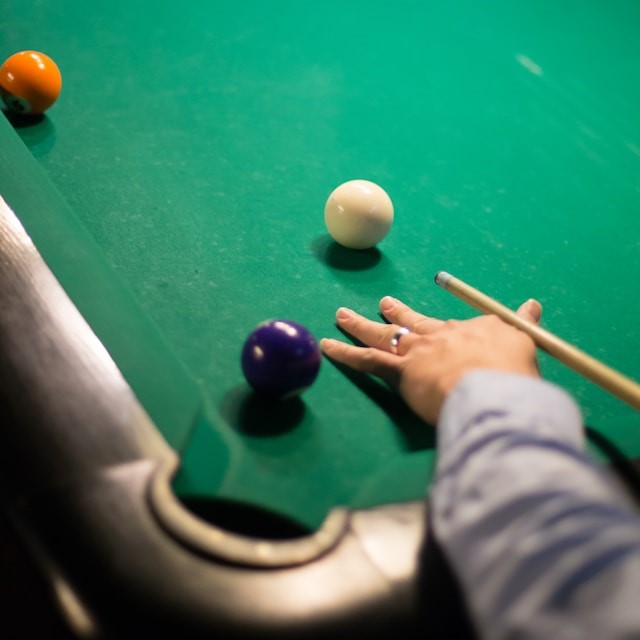 Hand holding pool cue at billiards table.