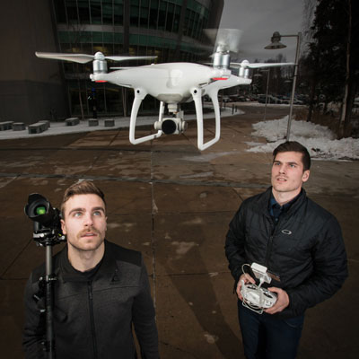 Two students observing a flying drone.