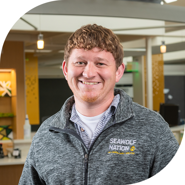 Admissions Counselor Casey Karn smiling at camera in front of Welcome to UAA kiosk.