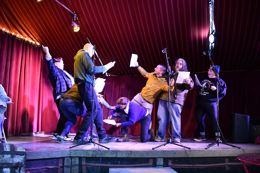 a group of actors on a stage in an outdoor theatre tent